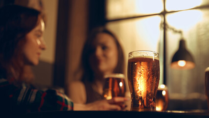 Cold beer glass standing on table in warm pub interior. Concept of beverage advertising, brewery product shots, bar lifestyle visuals, nightlife marketing materials, and refreshment-focused branding.