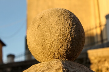 Close-up of a rough-textured stone or concrete sphere finial, bathed in the warm, golden light of the setting or rising sun, with a blurred background.
