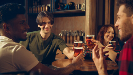 Group raising beer glasses together while relaxing at cozy pub table. Concept of bar campaigns, brewery advertising, beverage branding, nightlife scenes.