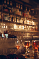 Beer being poured from bottle into glass at bar counter during evening service. Concept of beverage branding, bar advertising, brewery visuals, drink menu promotion.