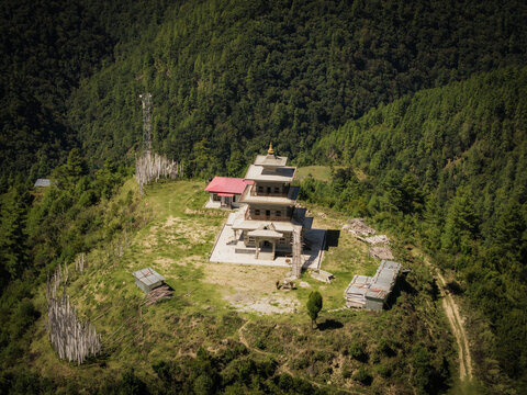 Aerial view of a tiered temple structure with a red roof stands prominently atop a lush, green hill overlooking the distant mountains, Rashigang, Paro, Bhutan.