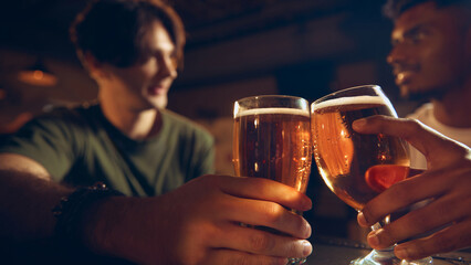 Closeup of beer glasses in hands during friendly toast at pub counter. Concept of beverage ads, brewery visuals, bar marketing materials, social drinking themes.