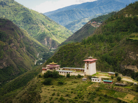 Aerial view of the majestic fortress-monastery perched amidst the verdant hills, its white walls and ochre roofs contrasting with the deep green valleys, Raga, Paro, Bhutan.