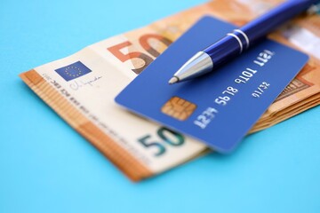 Credit card and pen with euro currency money bills banknotes on light blue background. Business, financial operations and accounting in European Union