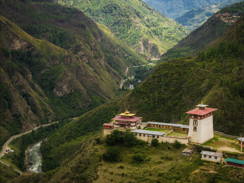 Aerial view of a monastery perched amidst verdant, rugged mountains, with a winding river snaking through the valley below, Raga, Paro, Bhutan.
