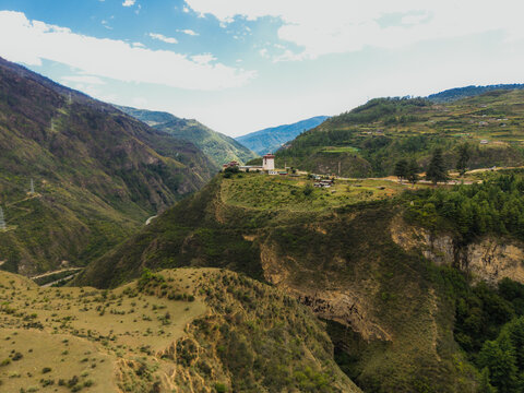 Aerial view of a temple standing atop a hill amidst the rugged, mountainous terrain, bathed in the soft light of the sun, Raga, Paro, Bhutan.