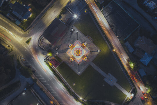Aerial view of the illuminated National Memorial Chorten radiates warmth against the cool night, framed by the flowing lights of surrounding traffic, Thimphu, Bhutan.