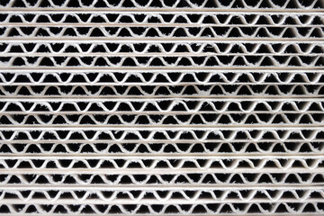 a detailed close-up shot of corrugated cardboard showing its wavy internal structure and repeating geometric pattern. The image highlight the raw, fibrous edges and rhythmic lines, creating an abstrac