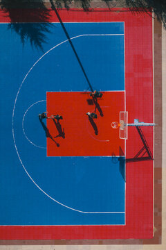 Aerial view of the vibrant red and blue basketball court, with the shadows of players stretching long, a game frozen in time, Thimphu, Bhutan.