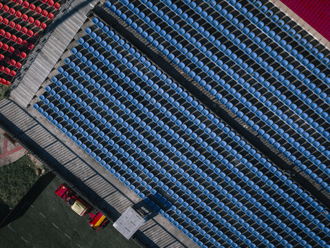 Aerial view of rows of blue stadium seats contrasted by the vibrant red seats and green grass, creating a striking geometric pattern, Thimphu, Bhutan.