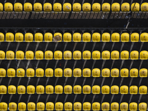 Aerial view of a stadium's bright yellow seats casting stark shadows across the concrete, creating a rhythmic pattern of light and dark, Thimphu, Bhutan.