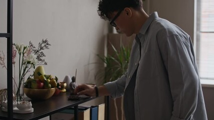 Medium handheld shot of young Asian man burning incense stick and praying in modern office workspace