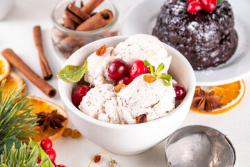 Christmas pudding ice cream, winter and Christmas traditional flavor, white vanilla gelato mixed with pudding, alcohol syrup, chocolate pieces, on white table with Christmas decor and English pudding