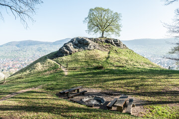 Runde Feuerstelle mit Natursteinen und Holzb&auml;nken vor H&uuml;gel Calverb&uuml;hl mit Felsen und   Laubbaum bei Dettingen an der Erms am Fu&szlig;e der schw&auml;bischen Alb.