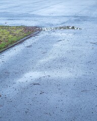 Wet asphalt road with puddle and grass border after rain