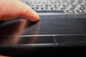 A close-up of a finger touching the matte touchpad of a black laptop. The image with shallow depth of field focuses on the user's interaction with the computer, symbolizing work, navigation, and the u