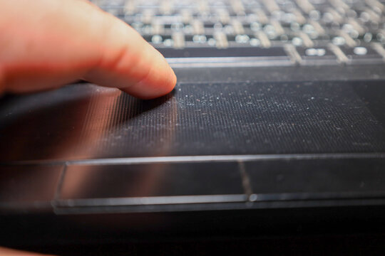 A close-up of a finger touching the matte touchpad of a black laptop. The image with shallow depth of field focuses on the user's interaction with the computer, symbolizing work, navigation, and the u