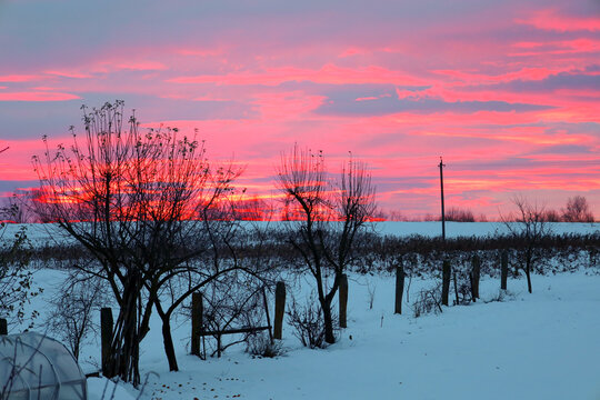 ​An intense, dramatic winter sunrise or sunset where the sky is ablaze with bright pink and red hues.