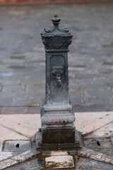 Obraz premium Old cast iron water fountain with decorative details and a small stream of water flowing, set on a stone pavement in Venice, Italy. Classic European street element.