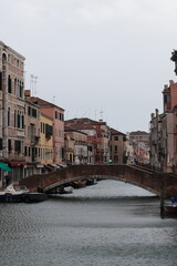 Scenic canal view in Venice with colorful old buildings, a stone bridge, and small boats on calm water, capturing the charm of traditional Italian architecture.
