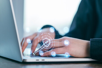 Hands typing on laptop keyboard while digital security icons hover above in a modern workspace