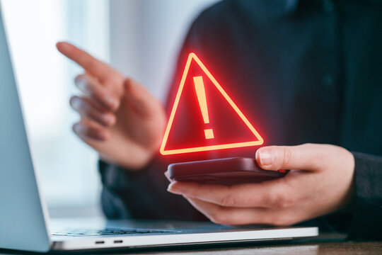 Person using smartphone while pointing at computer screen, highlighting important warning symbol