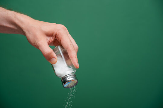 Human hand sprinkling white salt from shaker