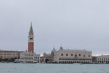 View of Venice with St. Mark’s Campanile and Doge’s Palace seen from the water under a cloudy sky, showing iconic Venetian architecture and calm lagoon scenery.