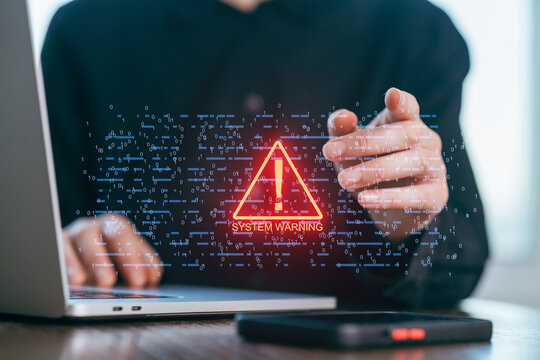 Person pointing at a warning sign on a laptop screen while working in a modern office setting