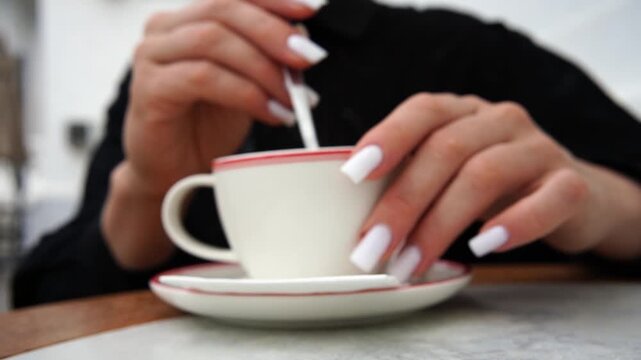 Woman, coffee, stirring, with white nails, stirs hot coffee in a cup and saucer, a relaxing morning ritual