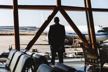 Man standing at airport window looking at airplane