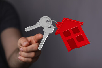 Close-up of a hand holding house keys with a red house charm, representing homeownership, property, or real estate.