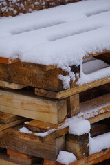 Zbliżenie na solidne, drewniane palety pokryte śniegiem. Widoczne szczeg&oacute;ły drewna i śnieżnej warstwy podkreślają fakturę i surowość materiał&oacute;w na budowie.