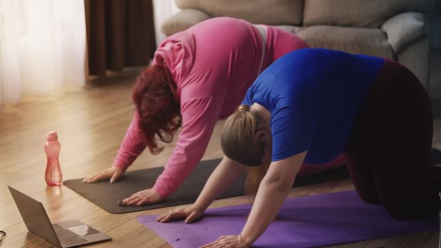 Curvy women stretching on yoga mat while watching fitness tutorial on screen - Powered by Adobe