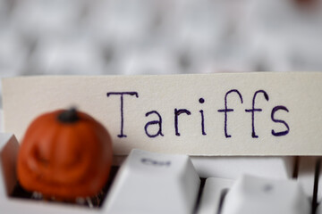 tariff written on paper, resting on a white keyboard with a blurred decorative miniature pumpkin. Depicts global trade, economics, and Halloween, seasonal finance