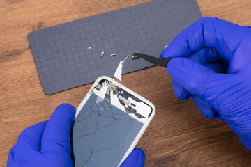 The master's hands use tweezers to remove glass fragments from the gadget's screen, close-up