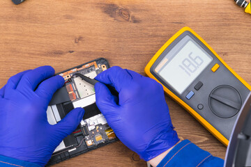 The master uses a voltage measuring device and tweezers to repair the phone display, close-up