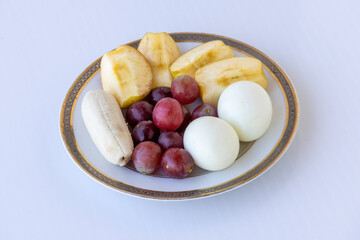 A ceramic plate holding a colorful and nutritious assortment of peeled apple slices, red grapes, banana, and two hard-boiled eggs; a healthy, high-protein breakfast or snack concept.