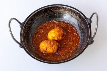 Spicy Egg Masala Curry, or Anda Curry (Dim Bhuna), a delicious traditional Bengali food dish of boiled eggs simmered in a rich, vibrant gravy, served in a karahi on a white background.