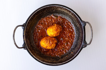 Close-up of traditional Bengali style Boiled Egg Masala Curry, or Anda Dim Bhuna, served in a rustic karahi on a white background. A popular, spicy and delicious South Asian meal. Top view.