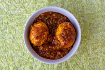 Delicious, homemade Spicy Egg Masala or Anda Curry (Dim Bhuna), a popular traditional Bengali dish, served hot in a white ceramic bowl. Asian Indian food concept. Top view.