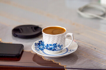 A cup of Turkish coffee, a mobile phone lens cover and a power cable on a work desk