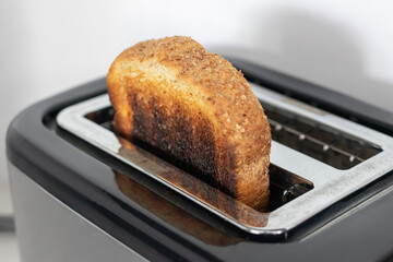 Burned whole grain toast popping from toaster, slightly smoking and crispy