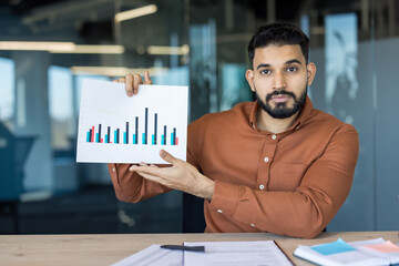 Young businessman presenting financial data chart, explaining analytics and trends, portraying business growth and market strategy from a modern office setting