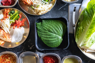 Perilla leaves and fresh lettuce with Korean side dishes and spicy sauces arranged for meal,...