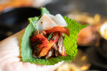 Korean grilled meat wrap with spicy kimchi and pickled radish on perilla leaf, hand held savory bite
