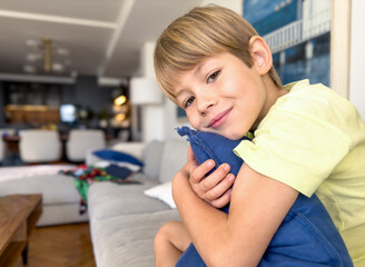Cute blond boy hugging a cushion while sitting on the couch at home