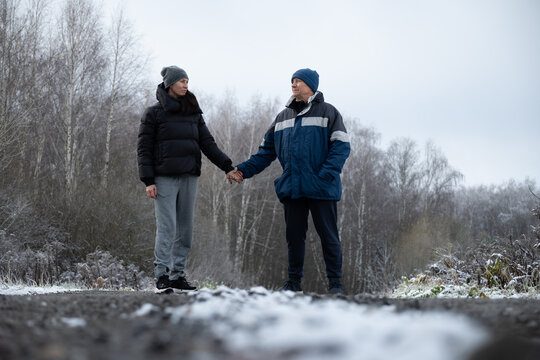 Two friends man and woman warmly dressed, holding hands while walking along snowy path in winter landscape. Cold season. Outdoor. Friendship, love and warmth on cold day.
