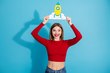 Smiling young woman holding a paper rocket against blue background conveying creativity and...