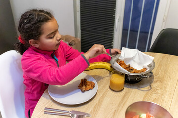 Young girl enjoying a meal at home, serving crispy fried chicken pieces onto her plate, promoting family dining, childhood, and diverse culture concepts